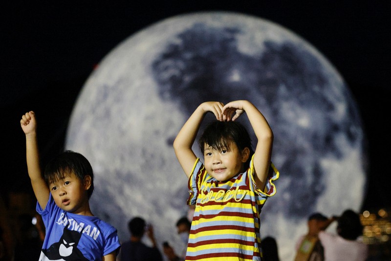 Seorang wanita berpose di depan balon raksasa berbentuk bulan menjelang Festival Pertengahan Musim Gugur, di Hong Kong, China 20 September 2021. (REUTERS/Tyrone Siu) A woman poses for a photo in front of a giant moon-shaped balloon ahead of Mid-Autumn Festival, in Hong Kong, China September 20, 2021. REUTERS/Tyrone Siu