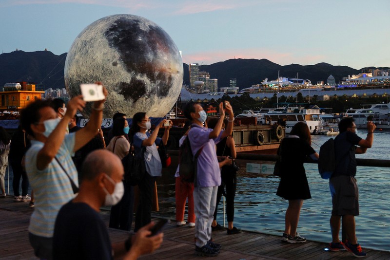 A woman poses for a photo in front of a giant moon-shaped balloon ahead of Mid-Autumn Festival, in Hong Kong, China September 20, 2021. REUTERS/Tyrone Siu