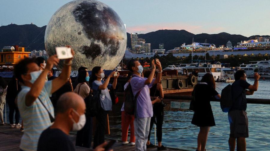 A woman poses for a photo in front of a giant moon-shaped balloon ahead of Mid-Autumn Festival, in Hong Kong, China September 20, 2021. REUTERS/Tyrone Siu