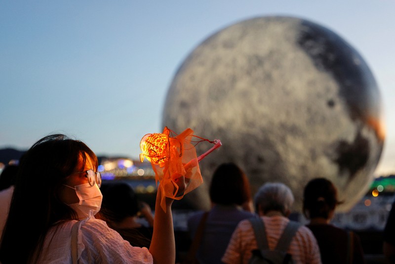 Seorang wanita berpose di depan balon raksasa berbentuk bulan menjelang Festival Pertengahan Musim Gugur, di Hong Kong, China 20 September 2021. (REUTERS/Tyrone Siu) A woman poses for a photo in front of a giant moon-shaped balloon ahead of Mid-Autumn Festival, in Hong Kong, China September 20, 2021. REUTERS/Tyrone Siu
