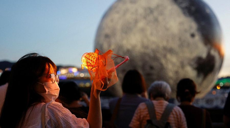 A woman poses for a photo in front of a giant moon-shaped balloon ahead of Mid-Autumn Festival, in Hong Kong, China September 20, 2021. REUTERS/Tyrone Siu