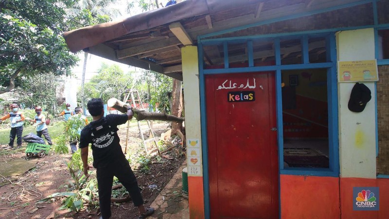 Sejumlah relawan dibantu para guru sekolah alam saat melakukan evakuasi pohon tumbang akibat puting beliung di Depok, Jawa Barat, Rabu 22 September 2021. Kawasan Depok dilanda hujan angin hingga hujan es di daerah Beji, Kota Depok kemarin (21/9) sore. Akibat hujan angin di Depok, pohon tumbang pun tak bisa dielakkan. Berdasarkan data Pemadam Kebakaran (Damkar), setidaknya ada enam lokasi pohon tumbang di Depok. Sejumlah relawan hingga kini mengevakuasi potongan pohon yg menimpa bagian yang rusak  kanopi. Akibat kejadian tersebut proses kegiatan belajar mengajar untuk sementara diberhentikan. Salah satu guru di sekolah alam, Ode mengatakan tidak ada korban jiwa. Kerugian hanya materil dan  pohon yang menimpa atap sekolah. (CNBC Indonesia/ Muhammad Sabki)