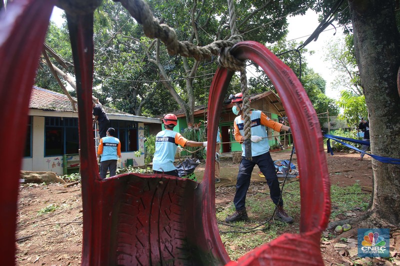 Sejumlah relawan dibantu para guru sekolah alam saat melakukan evakuasi pohon tumbang akibat puting beliung di Depok, Jawa Barat, Rabu 22 September 2021. Kawasan Depok dilanda hujan angin hingga hujan es di daerah Beji, Kota Depok kemarin (21/9) sore. Akibat hujan angin di Depok, pohon tumbang pun tak bisa dielakkan. Berdasarkan data Pemadam Kebakaran (Damkar), setidaknya ada enam lokasi pohon tumbang di Depok. Sejumlah relawan hingga kini mengevakuasi potongan pohon yg menimpa bagian yang rusak  kanopi. Akibat kejadian tersebut proses kegiatan belajar mengajar untuk sementara diberhentikan. Salah satu guru di sekolah alam, Ode mengatakan tidak ada korban jiwa. Kerugian hanya materil dan  pohon yang menimpa atap sekolah. (CNBC Indonesia/ Muhammad Sabki)