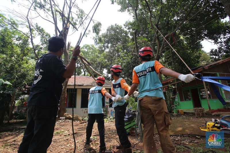 Puting beliung akibat curah hujan tinggi di Depok Sejumlah relawan dibantu para guru sekolah alam saat melakukan evakuasi pohon tumbang akibat puting beliung di Depok, Jawa Barat, Rabu 22 September 2021. Kawasan Depok dilanda hujan angin hingga hujan es di daerah Beji, Kota Depok kemarin (21/9) sore. Akibat hujan angin di Depok, pohon tumbang pun tak bisa dielakkan. Berdasarkan data Pemadam Kebakaran (Damkar), setidaknya ada enam lokasi pohon tumbang di Depok. Sejumlah relawan hingga kini mengevakuasi potongan pohon yg menimpa bagian yang rusak kanopi. Akibat kejadian tersebut proses kegiatan belajar mengajar untuk sementara diberhentikan. Salah satu guru di sekolah alam, Ode mengatakan tidak ada korban jiwa. Kerugian hanya materil dan pohon yang menimpa atap sekolah. (CNBC Indonesia/ Muhammad Sabki)