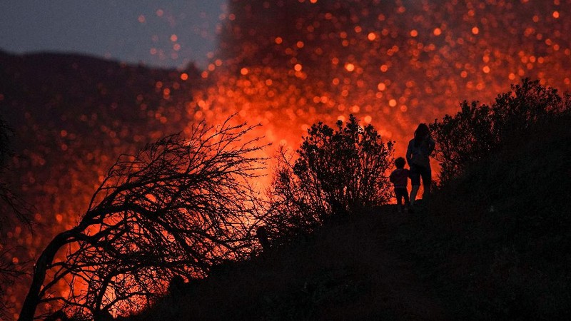 A woman climbs a hill with a child to see the Cumbre Vieja volcano as it continues to erupt in Tacande de Arriba on the Canary Island of La Palma, Spain, October 2, 2021. REUTERS/Juan Medina     TPX IMAGES OF THE DAY