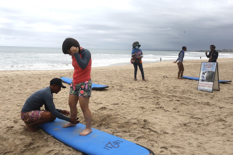 Virus Outbreak Indonesia A surf instructor prepares for surf lesson to a tourist at Kuta beach, Bali, Indonesia on Wednesday, Oct. 6, 2021. Indonesia plans to reopen the airport in the resort island of Bali for international flights on Oct. 14, after closing it for more than a year because of the COVID-19 pandemic. (AP Photo/Firdia Lisnawati)