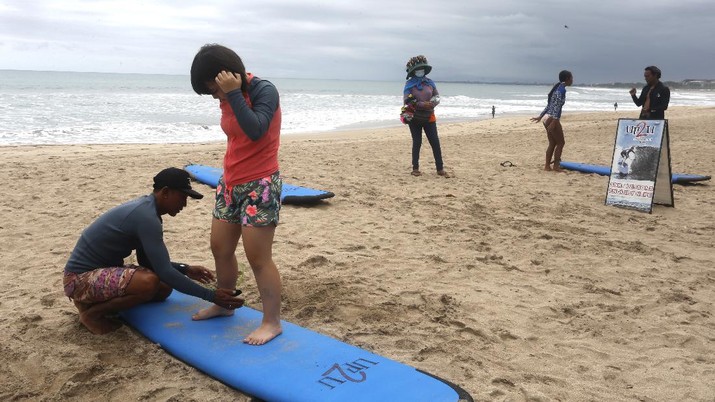 Virus Outbreak Indonesia A surf instructor prepares for surf lesson to a tourist at Kuta beach, Bali, Indonesia on Wednesday, Oct. 6, 2021. Indonesia plans to reopen the airport in the resort island of Bali for international flights on Oct. 14, after closing it for more than a year because of the COVID-19 pandemic. (AP Photo/Firdia Lisnawati)