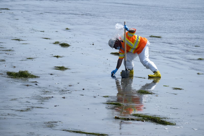 California Oil Spill People play on the sand in the background as workers in protective suits clean the contaminated beach after an oil spill in Newport Beach, Calif., on Wednesday, Oct. 6, 2021. A major oil spill off the coast of Southern California fouled popular beaches and killed wildlife while crews scrambled Sunday, to contain the crude before it spread further into protected wetlands. (AP Photo/Ringo H.W. Chiu)