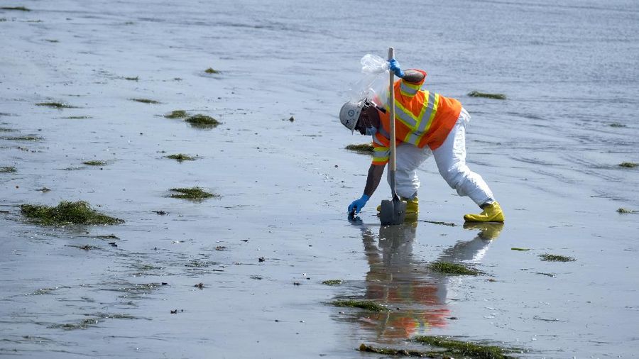 People play on the sand in the background as workers in protective suits clean the contaminated beach after an oil spill in Newport Beach, Calif., on Wednesday, Oct. 6, 2021. A major oil spill off the coast of Southern California fouled popular beaches and killed wildlife while crews scrambled Sunday, to contain the crude before it spread further into protected wetlands. (AP Photo/Ringo H.W. Chiu)