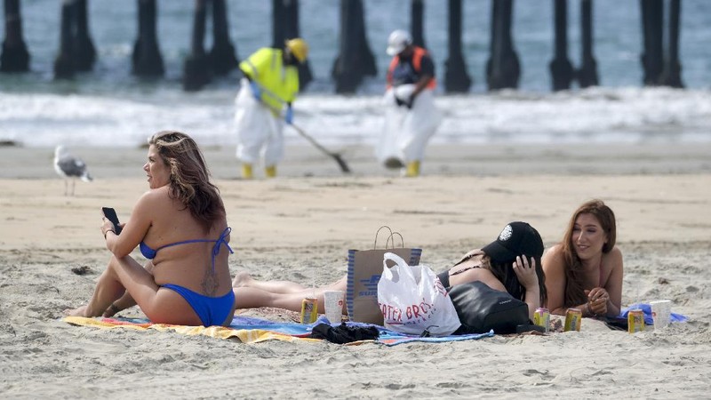 People play on the sand in the background as workers in protective suits clean the contaminated beach after an oil spill in Newport Beach, Calif., on Wednesday, Oct. 6, 2021. A major oil spill off the coast of Southern California fouled popular beaches and killed wildlife while crews scrambled Sunday, to contain the crude before it spread further into protected wetlands. (AP Photo/Ringo H.W. Chiu)