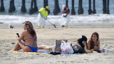 Beach goers are seen as workers in protective suits clean the contaminated beach after an oil spill, Wednesday, Oct. 6, 2021 in Newport Beach, Calif. A major oil spill off the coast of Southern California fouled popular beaches and killed wildlife while crews scrambled Sunday, to contain the crude before it spread further into protected wetlands. (AP Photo/Ringo H.W. Chiu)