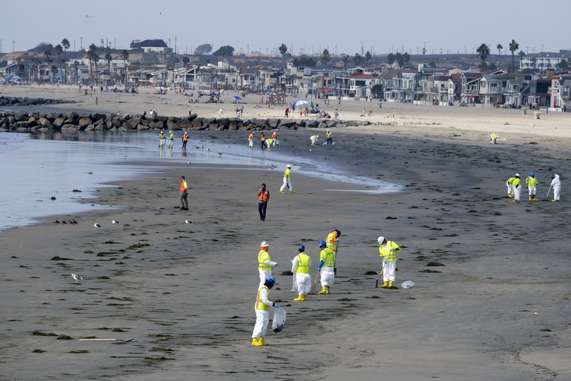 California Oil Spill People play on the sand in the background as workers in protective suits clean the contaminated beach after an oil spill in Newport Beach, Calif., on Wednesday, Oct. 6, 2021. A major oil spill off the coast of Southern California fouled popular beaches and killed wildlife while crews scrambled Sunday, to contain the crude before it spread further into protected wetlands. (AP Photo/Ringo H.W. Chiu)