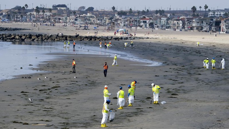 People play on the sand in the background as workers in protective suits clean the contaminated beach after an oil spill in Newport Beach, Calif., on Wednesday, Oct. 6, 2021. A major oil spill off the coast of Southern California fouled popular beaches and killed wildlife while crews scrambled Sunday, to contain the crude before it spread further into protected wetlands. (AP Photo/Ringo H.W. Chiu)