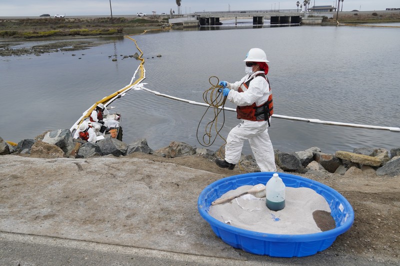 People play on the sand in the background as workers in protective suits clean the contaminated beach after an oil spill in Newport Beach, Calif., on Wednesday, Oct. 6, 2021. A major oil spill off the coast of Southern California fouled popular beaches and killed wildlife while crews scrambled Sunday, to contain the crude before it spread further into protected wetlands. (AP Photo/Ringo H.W. Chiu)