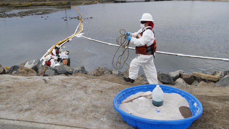 People play on the sand in the background as workers in protective suits clean the contaminated beach after an oil spill in Newport Beach, Calif., on Wednesday, Oct. 6, 2021. A major oil spill off the coast of Southern California fouled popular beaches and killed wildlife while crews scrambled Sunday, to contain the crude before it spread further into protected wetlands. (AP Photo/Ringo H.W. Chiu)
