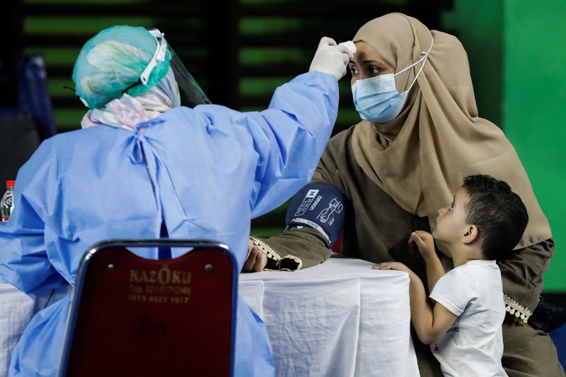A woman undergoes a health screening before receiving a dose of a vaccine against the coronavirus disease (COVID-19) during a mass vaccination program for asylum seekers and refugees at a sports hall in Jakarta, Indonesia, October 7, 2021. REUTERS/Ajeng Dinar Ulfiana