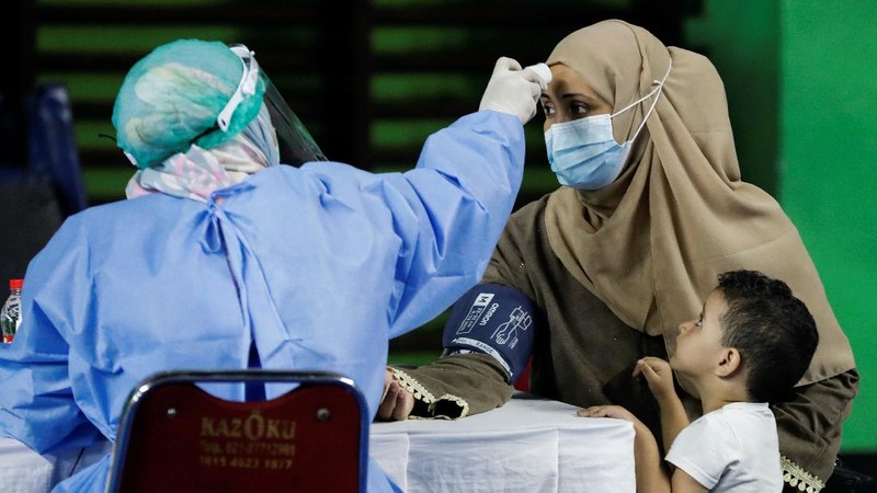 A woman undergoes a health screening before receiving a dose of a vaccine against the coronavirus disease (COVID-19) during a mass vaccination program for asylum seekers and refugees at a sports hall in Jakarta, Indonesia, October 7, 2021. REUTERS/Ajeng Dinar Ulfiana