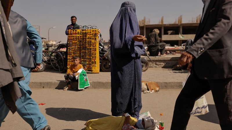 An Afghan woman wearing a burqa begs while taking care of her daughter in Kabul, Afghanistan October 7, 2021. Picture taken October 7, 2021. REUTERS/Jorge Silva