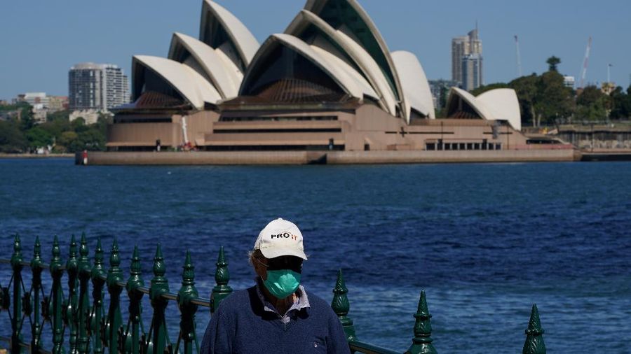FILE PHOTO: A person in protective face mask walks along the harbour waterfront across from the Sydney Opera House during a lockdown to curb the spread of coronavirus disease (COVID-19) outbreak in Sydney, Australia, October 6, 2021. REUTERS/Loren Elliott/File Photo