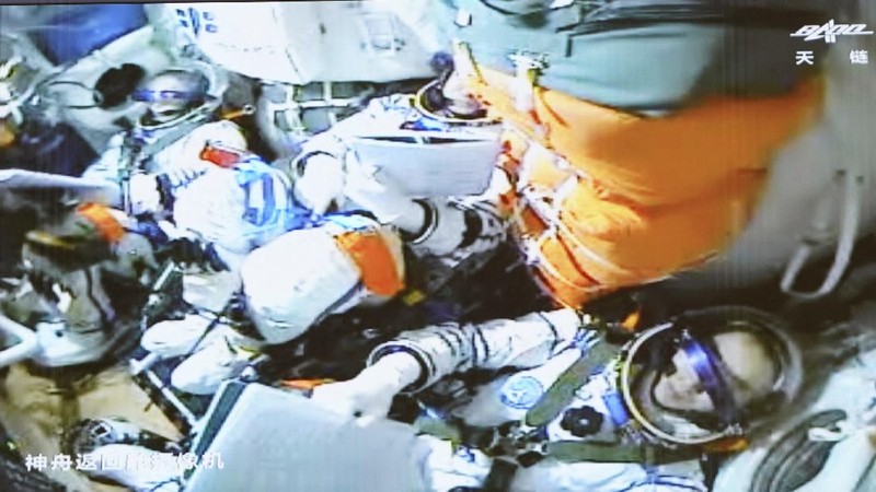 In this photo released by Xinhua News Agency, screen image captured at Beijing Aerospace Control Center in Beijing, China, Saturday, Oct. 16, 2021 shows three Chinese astronauts, from left, Ye Guangfu, Zhai Zhigang and Wang Yaping waving after entering the space station core module Tianhe. China's Shenzhou-13 spacecraft carrying three Chinese astronauts on Saturday docked at its space station, kicking off a record-setting six-month stay as the country moves toward completing the new orbiting outpost. Chinese characters,  left, read 