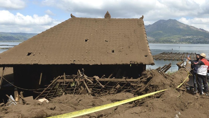 A woman walks past houses by Lake Batur which were damaged by an earthquake-triggered landslide in Bangli, on the island of Bali, Indonesia, Saturday, Oct. 16, 2021. A few people were killed and another several were injured when a moderately strong earthquake and an aftershock hit the island early Saturday. (AP Photo/Dewa Raka)
