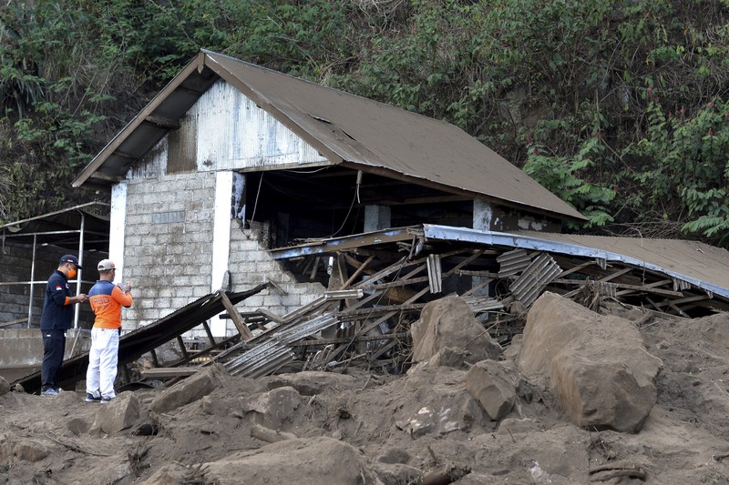 A woman walks past houses by Lake Batur which were damaged by an earthquake-triggered landslide in Bangli, on the island of Bali, Indonesia, Saturday, Oct. 16, 2021. A few people were killed and another several were injured when a moderately strong earthquake and an aftershock hit the island early Saturday. (AP Photo/Dewa Raka)