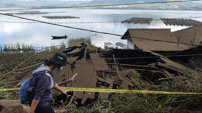 A woman walks past houses by Lake Batur which were damaged by an earthquake-triggered landslide in Bangli, on the island of Bali, Indonesia, Saturday, Oct. 16, 2021. A few people were killed and another several were injured when a moderately strong earthquake and an aftershock hit the island early Saturday. (AP Photo/Dewa Raka)