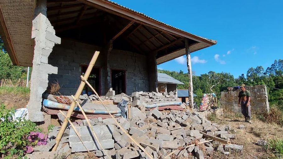 A woman walks past houses by Lake Batur which were damaged by an earthquake-triggered landslide in Bangli, on the island of Bali, Indonesia, Saturday, Oct. 16, 2021. A few people were killed and another several were injured when a moderately strong earthquake and an aftershock hit the island early Saturday. (AP Photo/Dewa Raka)