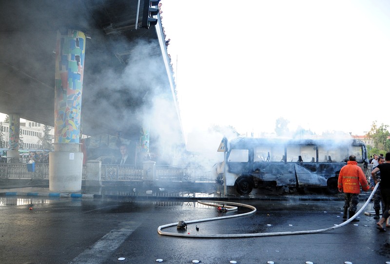A civil defense member hoses down a bus at the site of a roadside bomb attack in central Damascus, Syria, in this handout released by SANA October 20, 2021. SANA/Handout via REUTERS ATTENTION EDITORS - THIS IMAGE WAS PROVIDED BY A THIRD PARTY.  REUTERS IS UNABLE TO INDEPENDENTLY VERIFY THIS IMAGE.