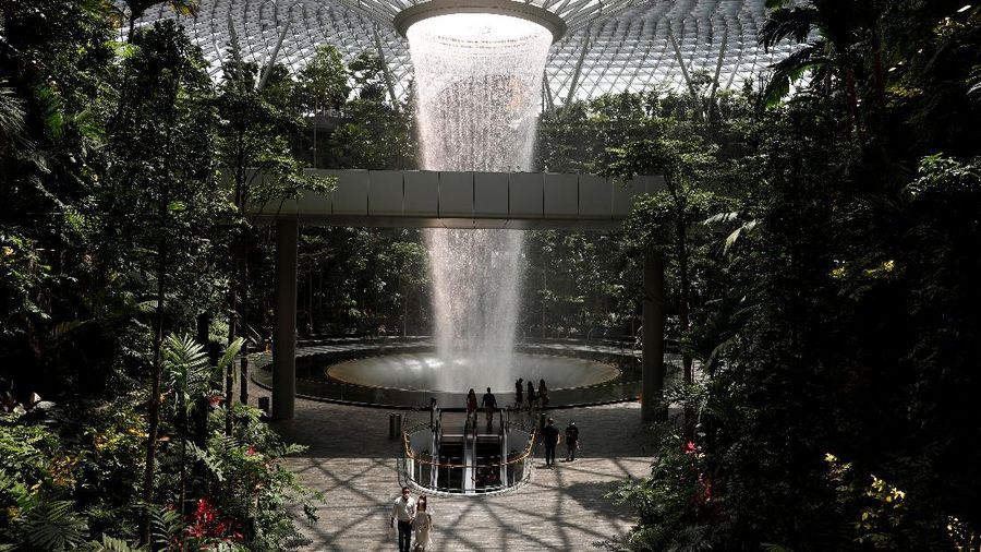 People walk past an indoor waterfall at Jewel Changi Airport in Singapore October 7, 2021. REUTERS/Edgar Su