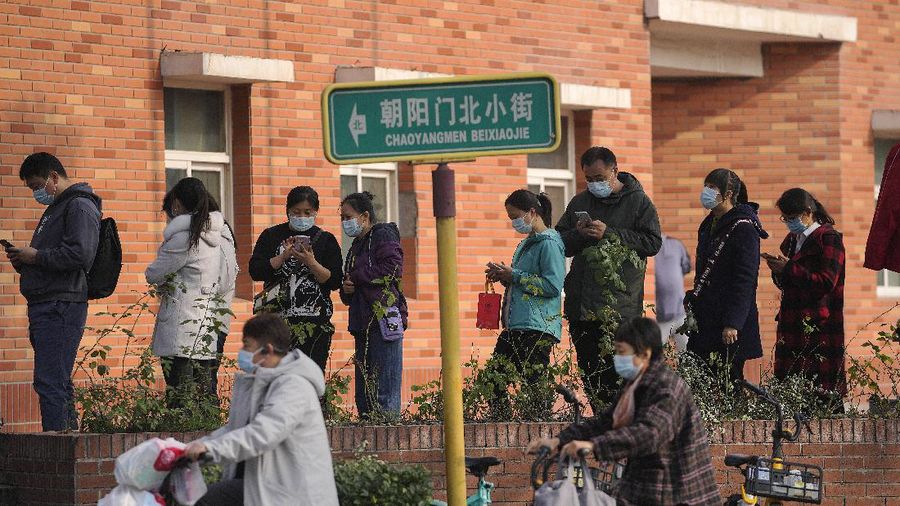 Women wearing face masks to help curb the spread of the coronavirus ride scooters passing by masked residents line up to receive booster shots against COVID-19 at a vaccination site in Beijing, Monday, Oct. 25, 2021. A northwestern Chinese province heavily dependent on tourism closed all tourist sites Monday after finding new COVID-19 cases. (AP Photo/Andy Wong)