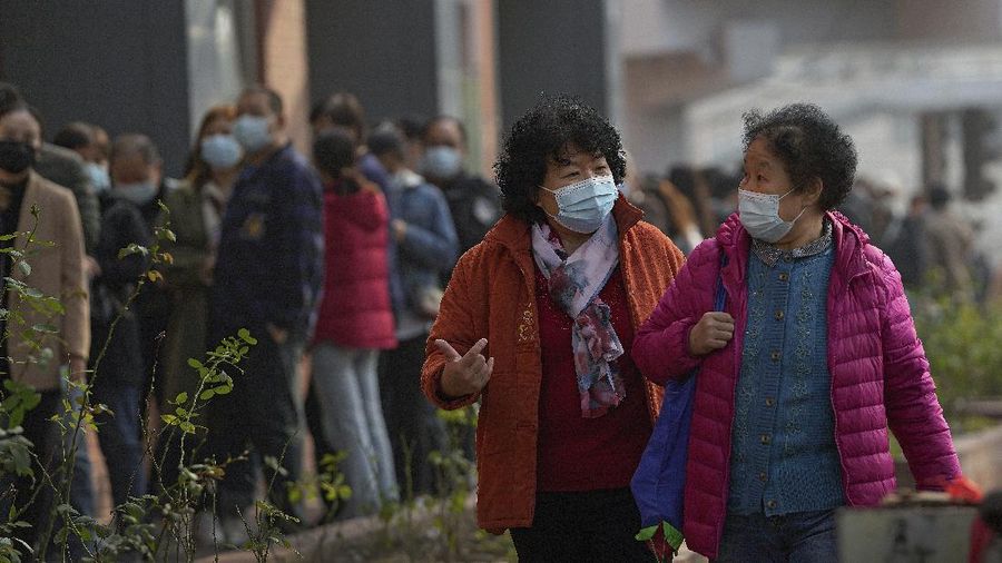 Women wearing face masks to help curb the spread of the coronavirus chat each other as they walk by masked residents line up to receive booster shots against COVID-19 at a vaccination site in Beijing, Monday, Oct. 25, 2021. A northwestern Chinese province heavily dependent on tourism closed all tourist sites Monday after finding new COVID-19 cases. (AP Photo/Andy Wong)