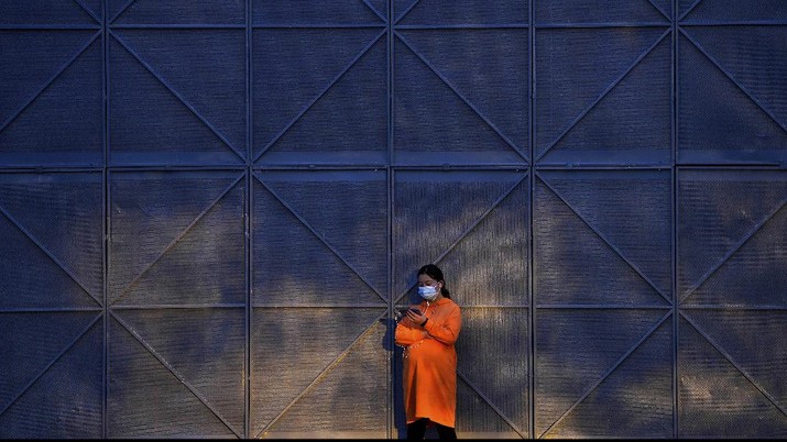 A pregnant woman wearing a face mask to help curb the spread of the coronavirus uses her smartphone as she sunbathes next to the steel frames at a construction site in Beijing, Wednesday, Oct. 27, 2021. (AP Photo/Andy Wong)