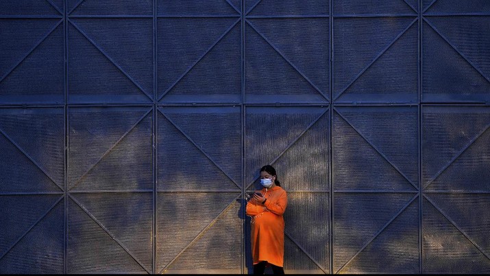 APTOPIX Virus Outbreak China A pregnant woman wearing a face mask to help curb the spread of the coronavirus uses her smartphone as she sunbathes next to the steel frames at a construction site in Beijing, Wednesday, Oct. 27, 2021. (AP Photo/Andy Wong)