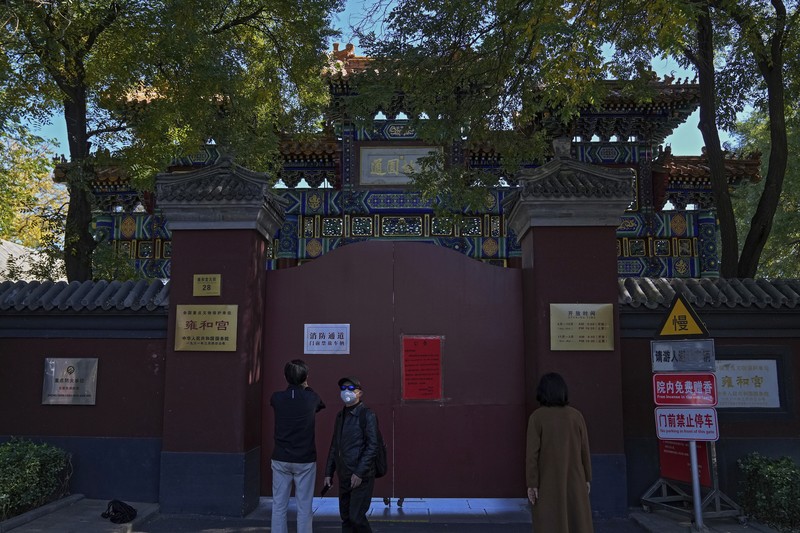 Virus Outbreak China Residents wearing face masks to help curb the spread of the coronavirus walk by a foreigner look at a red notice that reads: