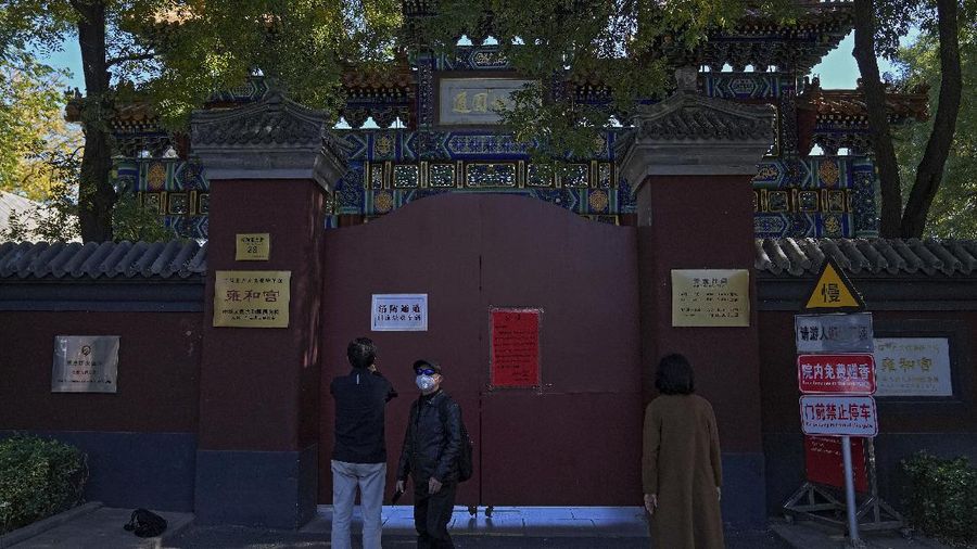 Residents wearing face masks to help curb the spread of the coronavirus walk by a foreigner look at a red notice that reads: 
