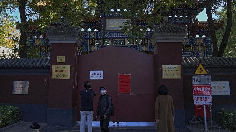Residents wearing face masks to help curb the spread of the coronavirus walk by a foreigner look at a red notice that reads: 
