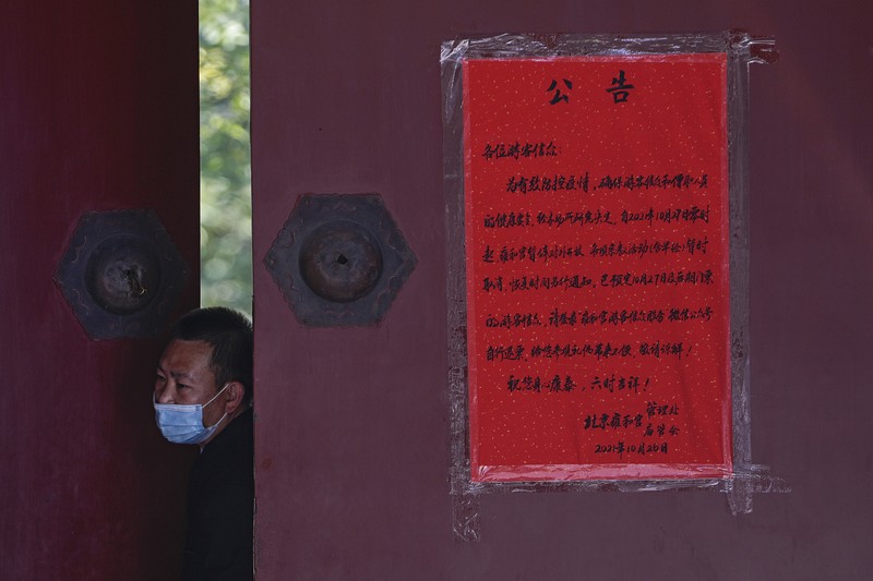Residents wearing face masks to help curb the spread of the coronavirus walk by a foreigner look at a red notice that reads: 
