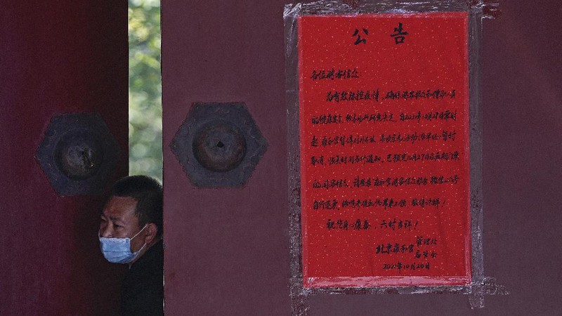 Residents wearing face masks to help curb the spread of the coronavirus walk by a foreigner look at a red notice that reads: 