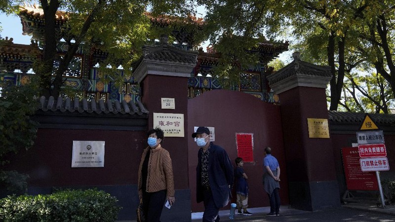Residents wearing face masks to help curb the spread of the coronavirus walk by a foreigner look at a red notice that reads: 