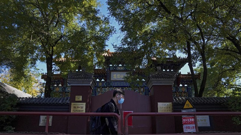 Residents wearing face masks to help curb the spread of the coronavirus walk by a foreigner look at a red notice that reads: 