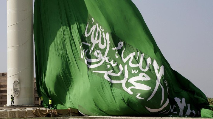 Workers take down a giant Saudi flag, that measures 49.5 meters by 33 meters (162 feet by 108 feet) for weekly maintenance, from what is believed to be the tallest flagpole in the world and one of Jiddah's landmarks, at King Abdullah Square, in Jiddah, Saudi Arabia, Thursday, Jan. 28, 2021. An Islamic creed reads, 