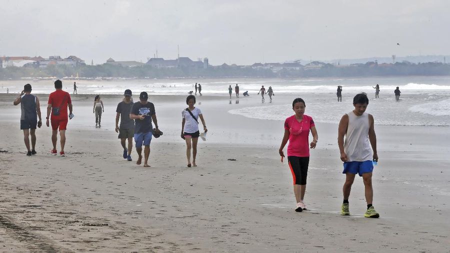 People walk along the beach in Kuta, Bali, Indonesia on Thursday, Oct. 28, 2021. After a summer where COVID-19 infection and death rates soared, officials said this week that they are sticking to plans to allow travel with some limitations, and expects nearly 20 million people to vacation in the popular islands of Java and Bali. (AP Photo/Firdia Lisnawati)