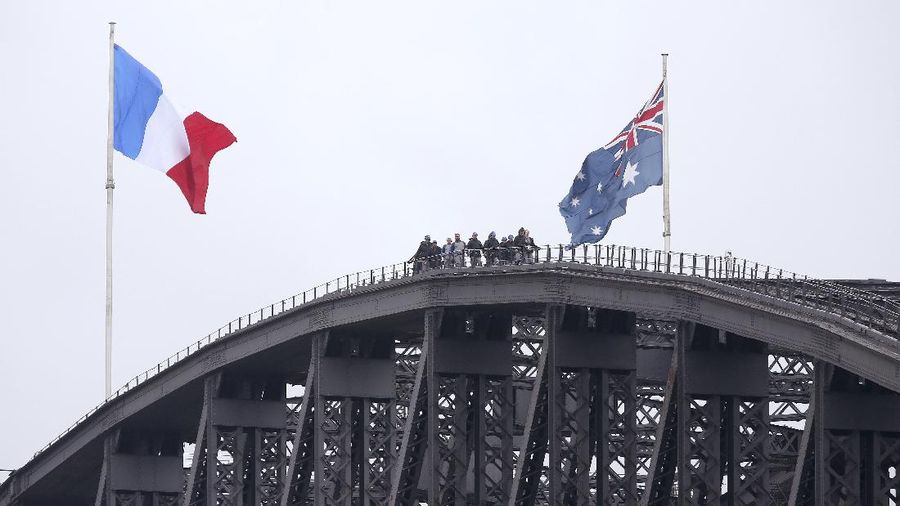 People walk along the top of the Sydney Harbour Bridge where a French flag, left, is flying alongside an Australian flag in Sydney, Sunday, Nov. 15, 2015. Australian Prime Minister Malcolm Turnbull extended Australia's deep sympathy to the people of France. 