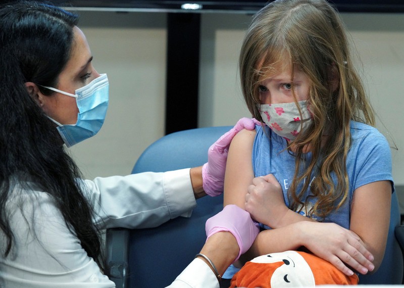Vaksin Covid-19 Untuk Anak di AS Nora Gossett, 7, reacts as she receives the Pfizer-BioNTech COVID-19 vaccine from Sophia Jan, MD, while her father Jeff Gossett, MD, holds her hand at Cohen Children's Medical Center as vaccines were approved for children aged 5-11, amid the coronavirus disease pandemic, in New Hyde Park, New York, U.S., November 4, 2021. REUTERS/Andrew Kelly