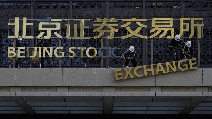 A man wearing a face mask looks back as workers installing the nameplate of the Beijing Stock Exchange on the Financial Street in Beijing, Sunday, Nov. 14, 2021. According the local news report, the Beijing Stock Exchange will start trading on Monday, Nov. 15. (AP Photo/Andy Wong)
