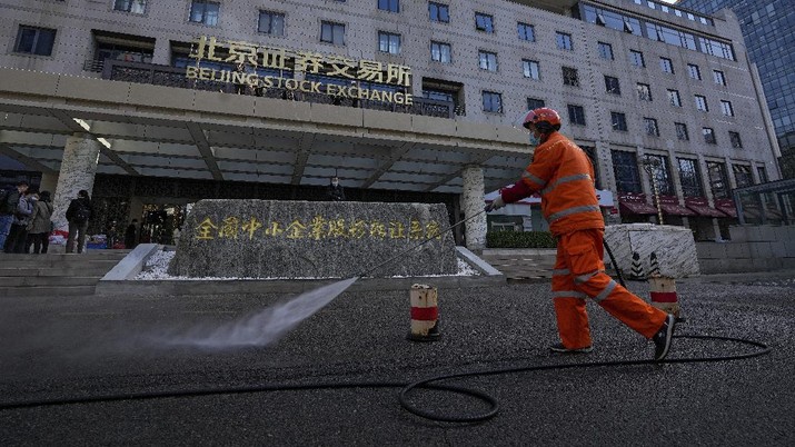 A man wearing a face mask looks back as workers installing the nameplate of the Beijing Stock Exchange on the Financial Street in Beijing, Sunday, Nov. 14, 2021. According the local news report, the Beijing Stock Exchange will start trading on Monday, Nov. 15. (AP Photo/Andy Wong)