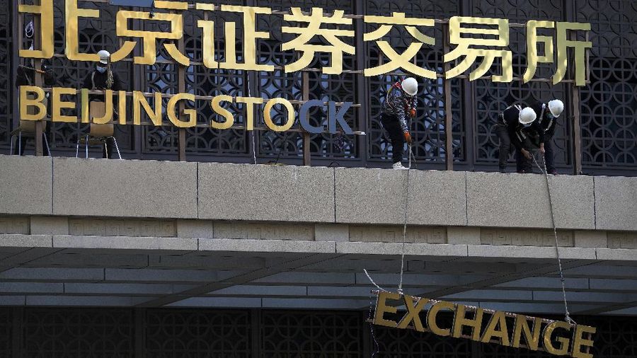 A man wearing a face mask looks back as workers installing the nameplate of the Beijing Stock Exchange on the Financial Street in Beijing, Sunday, Nov. 14, 2021. According the local news report, the Beijing Stock Exchange will start trading on Monday, Nov. 15. (AP Photo/Andy Wong)