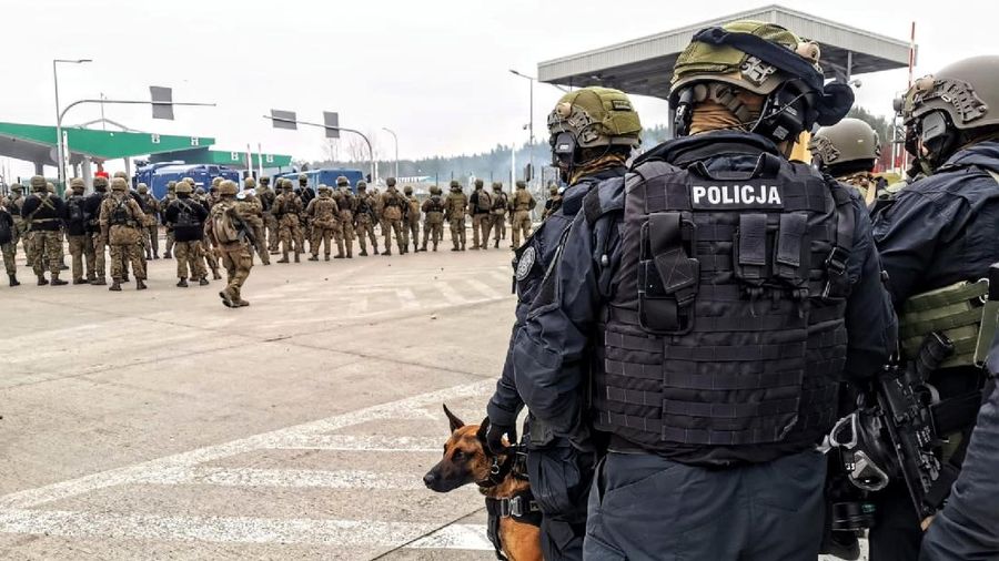 Polish law enforcement officers use water cannons, as migrants carry a log towards a fence at Kuznica - Bruzgi checkpoint, Poland, November 16, 2021. Policja Podlaska/Handout via REUTERS NO RESALES. NO ARCHIVES. MANDATORY CREDIT. THIS IMAGE HAS BEEN SUPPLIED BY A THIRD PARTY.