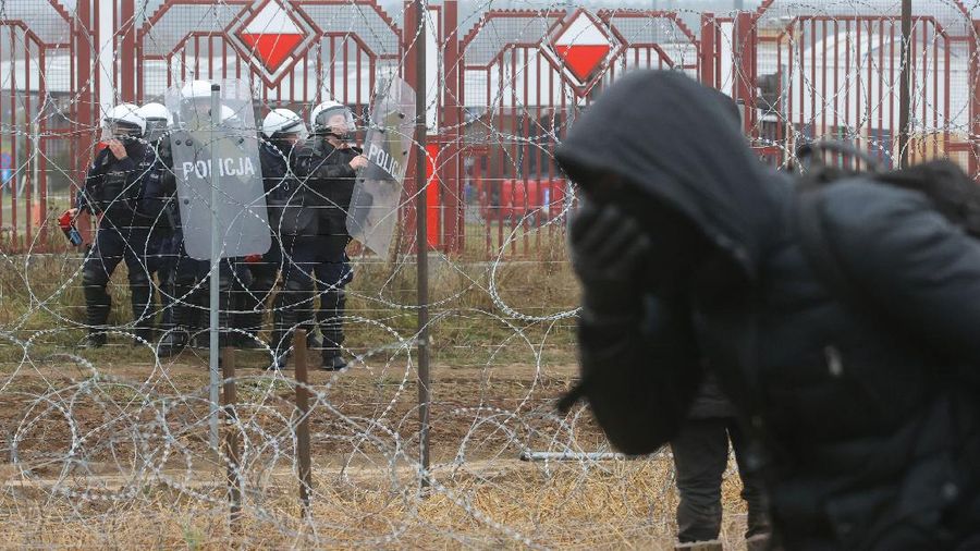 Polish law enforcement officers use water cannons, as migrants carry a log towards a fence at Kuznica - Bruzgi checkpoint, Poland, November 16, 2021. Policja Podlaska/Handout via REUTERS NO RESALES. NO ARCHIVES. MANDATORY CREDIT. THIS IMAGE HAS BEEN SUPPLIED BY A THIRD PARTY.